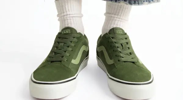 Zielone buty Vans na białym tle, widoczne od przodu, z nogawkami w białych skarpetkach i dżinsach.