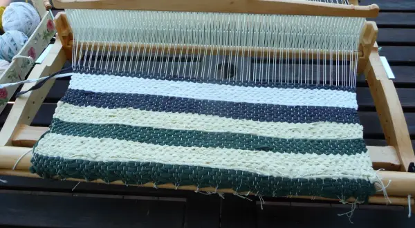 Krosno tkackie z częściowo utkanym, pasiastym chodnikiem ze szmatek w odcieniach zieleni, beżu i granatu.