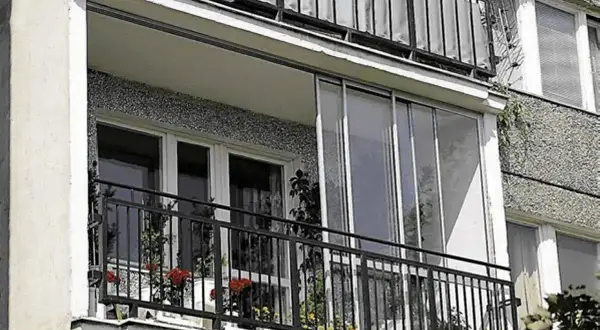 Zabudowany balkon w bloku z przeszklonymi drzwiami i oknami, idealny przykład jak zabudować balkon w bloku, by zyskać dodatkową przestrzeń.