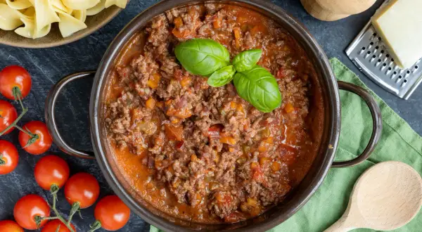 Herzhafte Bolognese-Sauce, perfekt für italienische Spaghetti-Rezepte. Frische Tomaten und Basilikum daneben.
