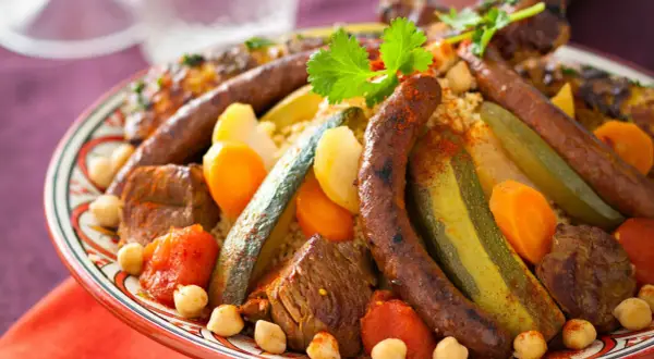 Un plat généreux de couscous royal, garni de merguez, de morceaux de viande, de légumes et de pois chiches, prêt à être dégusté.