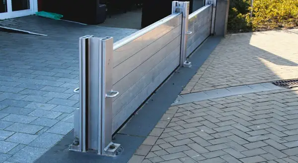 Moderne mobile Hochwasserschutzwand schützt das Haus vor Überschwemmungen. Sie ist aus Aluminium gefertigt und an den Pfosten befestigt.