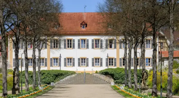 Prachtvolles Gebäude in Bad Bocklet, ideal für Ayurveda-Anwendungen. Ein Weg führt durch einen Garten mit Statuen und Blumen zum Eingang.
