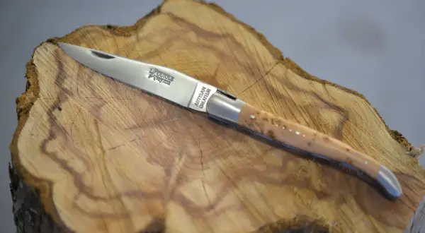 Navaja Laguiole artesanal, con mango de madera veteada y detalles plateados, reposa sobre un tocón de árbol.
