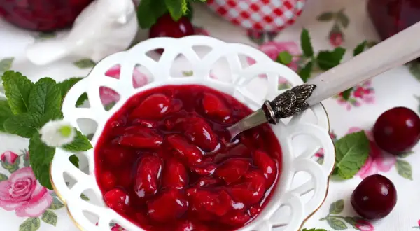 Aksamitna frużelina z wiśni w ozdobnej miseczce, ozdobiona miętą i świeżymi owocami.