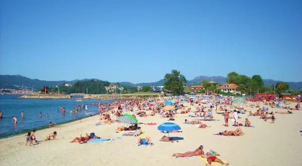 Día soleado en la playa Santa Marta de Baiona, con mucha gente disfrutando del mar y la arena bajo sombrillas.