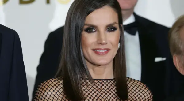 Elegancka królowa Letizia w czarnej, siateczkowej kreacji, z błyszczącymi oczami i uśmiechem, pozuje do zdjęcia z innymi osobami.