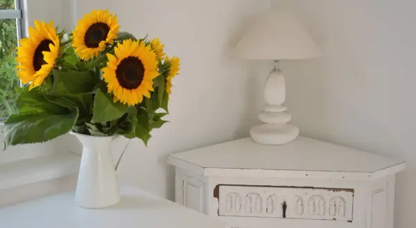 Strahlende sonnenblumen in der vase bringen Sommerstimmung in die Ecke, neben einer weißen Lampe auf einem antiken Schränkchen.
