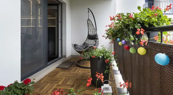 Un balcone accogliente con pavimento in legno, una sedia sospesa e fiori rossi. Un'idea per rivestire pavimento balcone fai da te.