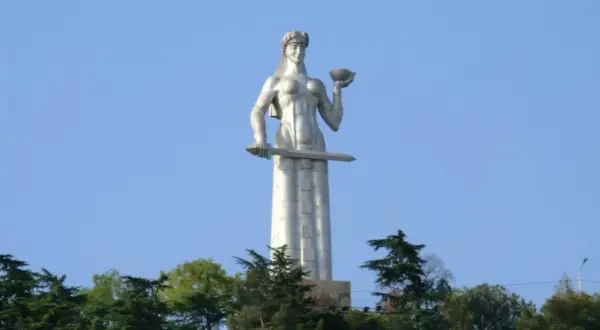 Matka Gruzja, symbol Tbilisi, trzyma miecz i puchar. Monumentalna postać wznosi się nad zielenią.