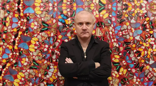Damien Hirst stoi przed ścianą ozdobioną jego dziełami z motyli.