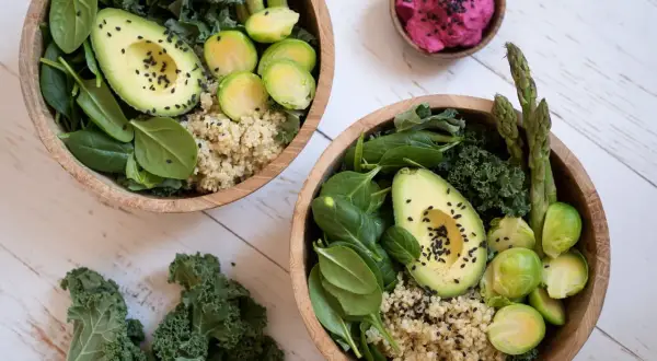 Två skålar med nyttig mat: quinoa, spenat, grönkål, avokado, brysselkål och sparris. En liten skål med rosa röra.