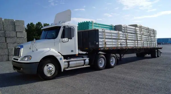 Camion blanc prêt pour le transport, avec un chargement de tuyaux blancs et verts bien sécurisé. L'arrimage des charges est essentiel pour un trajet sûr.