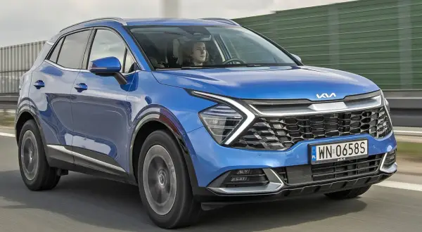 Niebieska, nowa Kia Sportage z kierowcą za kierownicą jedzie po drodze.