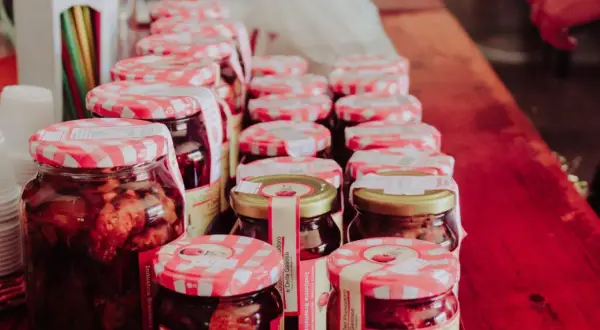 Słoiki z przetworami, w tym galaretką owocową, stoją w rzędzie. Zastanawiasz się, ile może stać galaretka owocowa w lodówce? Te domowe smakołyki wyglądają apetycznie.