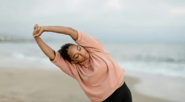 Femme en posture qi gong, s'étirant sur la plage au lever du soleil.