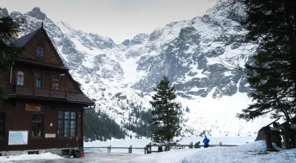 Maison en bois au pied des montagnes enneigées des Tatras en Pologne. Un lac gelé s'étend devant.