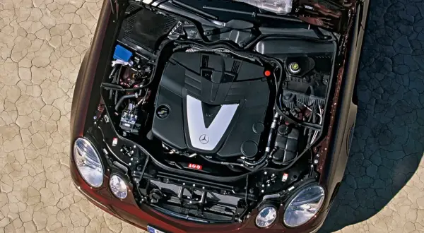 Silnik V6 om642 Mercedesa E-klasy, z otwartą maską, na tle spękanej ziemi.