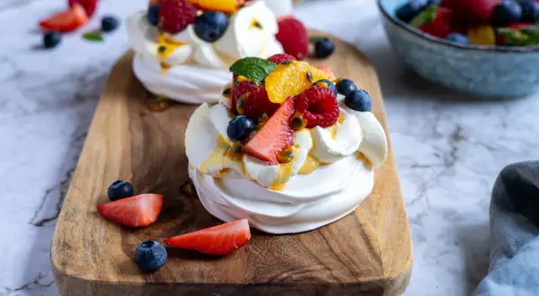 Två mini pavlovakakor med grädde och färska bär som jordgubbar, blåbär och hallon, toppade med passionsfrukt.