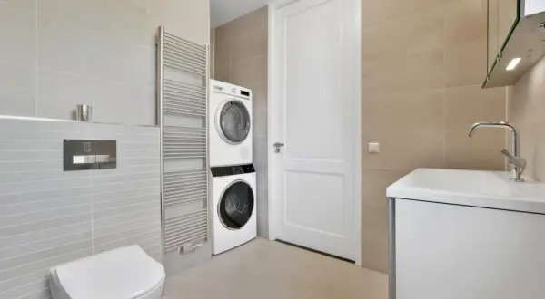 Bagno moderno con lavatrice e asciugatrice impilate, un termoarredo, un WC e un lavabo. Soluzione salvaspazio per nascondere lavatrice in bagno.