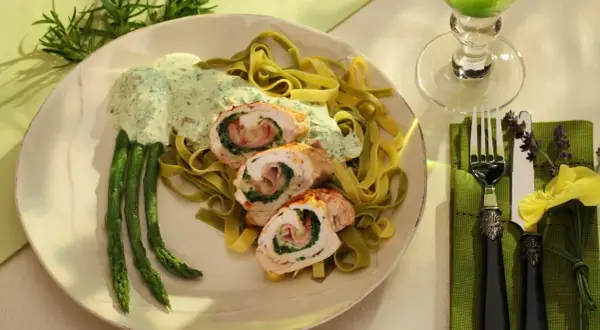Menu weselne dania gorące: roladki z kurczaka ze szpinakiem i szynką, podane z zielonym makaronem, szparagami i kremowym sosem.