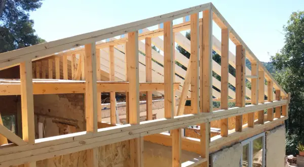 Estructura de madera para casa en construcción, con vigas y pilares de madera a la vista bajo un cielo azul.