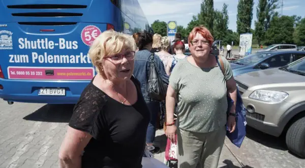Zwei Frauen warten auf den Shuttle-Bus zum Polenmarkt. Der blaue Bus wirbt mit "5€ Fahrpreis".