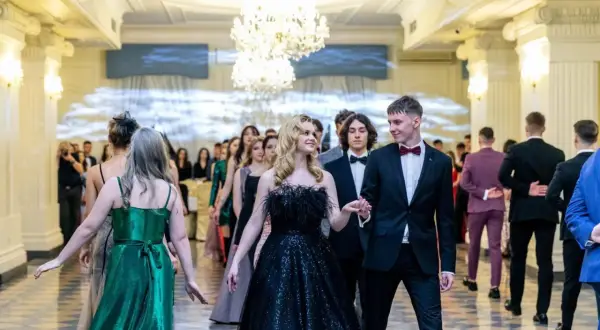 Elegancki strój do poloneza: para młodych ludzi w balowych kreacjach, otoczona przez innych uczestników balu.
