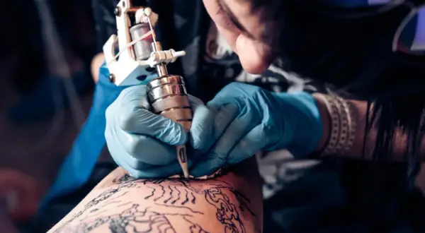 Artista creando un tatuaje de arte negro en la pierna.