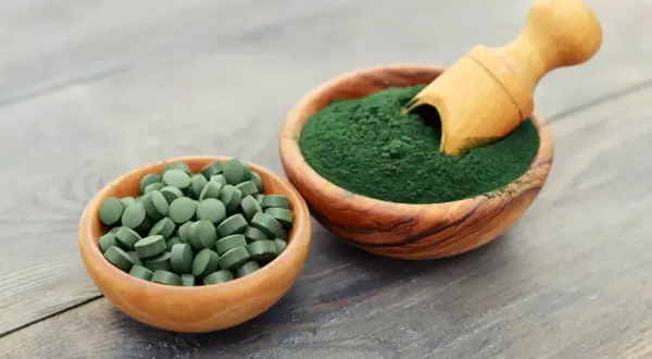 Chlorella i spirulina efekty: zielone tabletki i proszek w drewnianych miseczkach, gotowe do spożycia dla zdrowia.