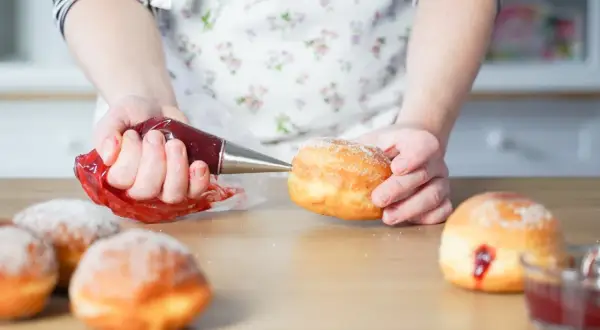 Hände füllen mit Marmelade gefüllte, zuckerbestäubte **bolas de fraile** mit einem Spritzbeutel.