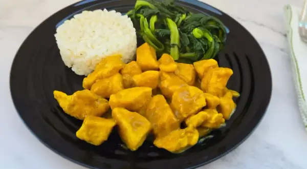 Piatto di pollo al curry con latte di cocco, riso bianco e verdure verdi saltate.