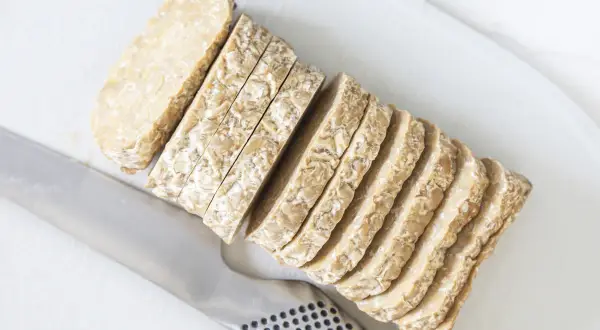 Pokrojony w plastry tempeh, czyli fermentowana soja, leży obok noża. To świetny składnik do wegańskich dań.