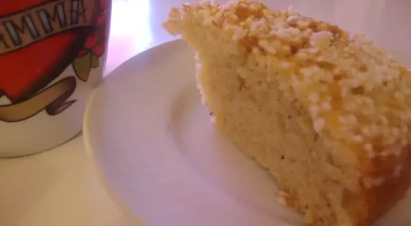 En bit gammaldags kardemummakaka med nötter på en vit tallrik, bredvid en mugg med texten "MAMMA".