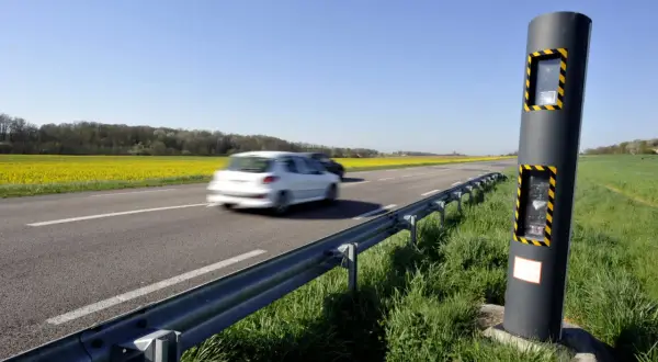 Un radar de vitesse sur le bord d'une route de campagne, avec des champs de colza jaunes et des voitures en mouvement. Ces photos des différents radars rappellent la vigilance.