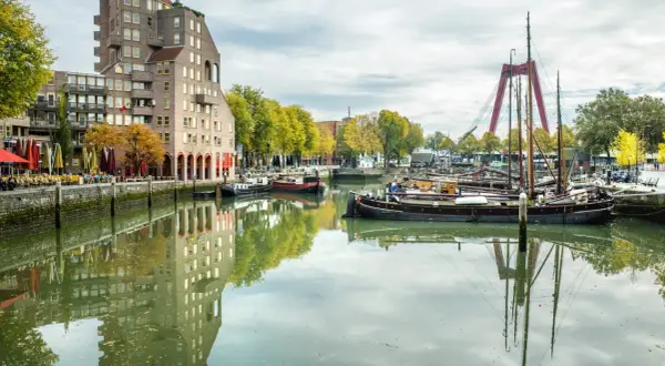 Widok na kanał z łodziami i nowoczesną architekturą, gdzie leży Rotterdam. W oddali czerwony most.