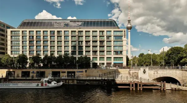 Nowoczesny budynek hotelu Radisson Blu Berlin nad rzeką Sprewą, z widoczną w tle wieżą telewizyjną.