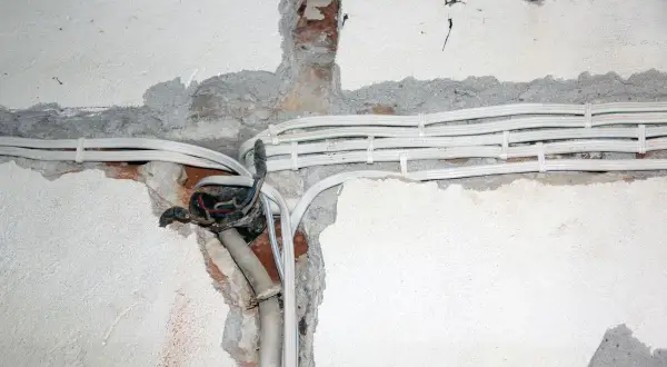 Widoczne przewody elektryczne w peszlach, częściowo ukryte w bruzdach w ścianie. Instalacja aluminiowa w trakcie prac.