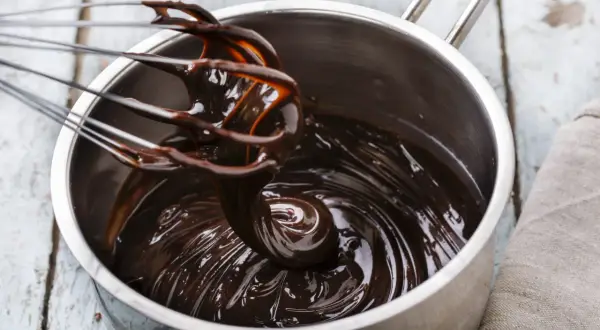 Fouet mélangeant du chocolat noir brillant dans une casserole, étape clé pour le tempérage.
