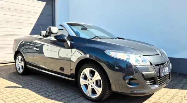 Ciemnoszary Renault cabrio z opuszczonym dachem, zaparkowany na wybrukowanym podjeździe przed budynkiem.