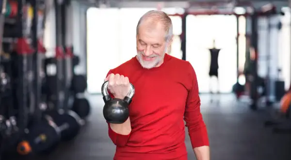 Ein älterer Mann trainiert mit einer Kettlebell. Ein guter Trainingsplan für Krafttraining ab 60 Jahren hält ihn fit.