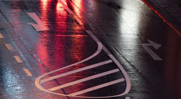 Nasse Straße mit roten und weißen Lichtreflexionen. Pfeile auf dem Asphalt zeigen die Fahrtrichtung an, wie bei einer anhalteweg formel.