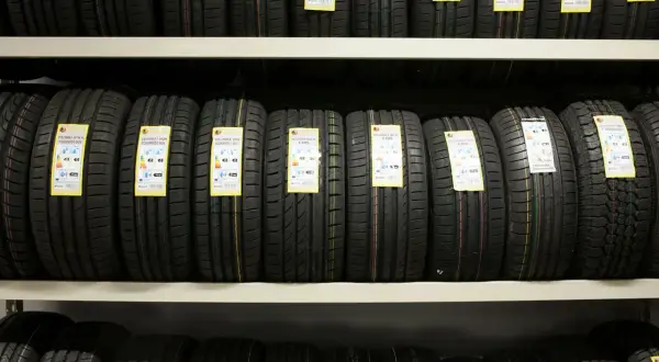 Rzędy nowych opon samochodowych na półkach sklepowych, z widocznymi etykietami informacyjnymi.