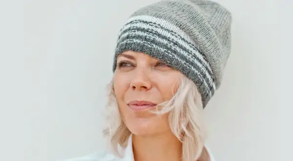 Frau mit blonden Haaren und Strickmütze, die nachdenklich in die Ferne blickt. Sie genießt ihr Leben mit 55 in Rente.