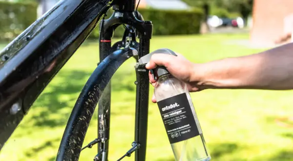 Hand sprüht Fahrradrahmen mit Reiniger ein. Sorgfältige Fahrrad Pflege für glänzende Ergebnisse im Freien.