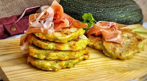 Deliciosas tortillitas de calabacín apiladas, coronadas con jamón serrano. Un plato fresco y sabroso.
