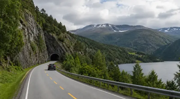 Svensk bil på väg mot en tunnel i Norge. Vacker bergig natur med sjö och moln.