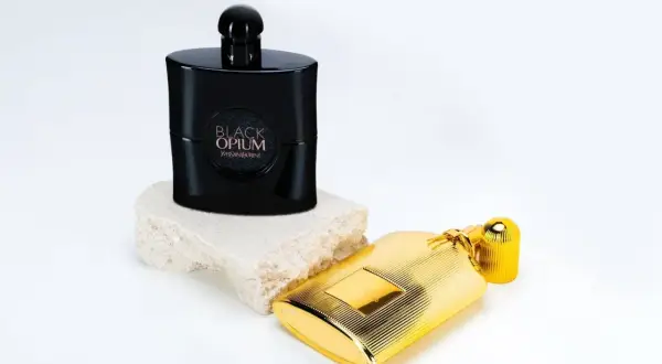Elegancki flakon Black Opium 90 ml na kamiennej podstawie obok złotego flakonu.