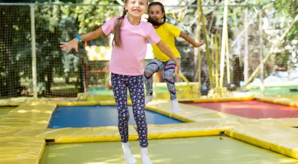 Dwie dziewczynki skaczą na trampolinie, śmiejąc się radośnie. Czy trampolina jest zdrowa dla dziewczynek? Z pewnością tak, to świetna zabawa i aktywność fizyczna!