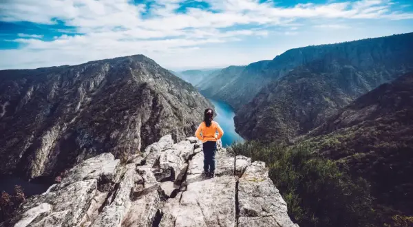 Niña en el mirador Vilouxe, contemplando un cañón con un río azul y montañas verdes bajo un cielo nublado.